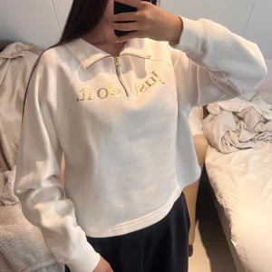 Vit Nike sweatshirt med guldtryck - Nike sweatshirt i vitt med guldig text 'Just do it.' och liten Swoosh på bröstet. Tröjan har half zip-dragkedja, hög krage och är långärmad. Mjuk insida och relaxed fit, perfekt för chill dagar eller träning.