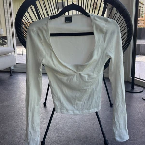 Vit långärmad topp från Gina Tricot - Säljer en vit långärmad topp från Gina Tricot med djup, rundad urringning. Toppen är i mjuk bomull och har en figurnära passform som passar perfekt till jeans eller kjol. Enkel och stilren design som är lätt att matcha.