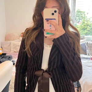 Brun kavaj - Säljer en brun kavaj från Hippocampe Paris perfekt till hösten!🍁Med vertikala ränder och snygg rosett i satinband framtill. Jackan har klassisk krage, långärmad passform och är gjord i mjuk manchester. Perfekt för dig som vill ha en cool och unik look!!