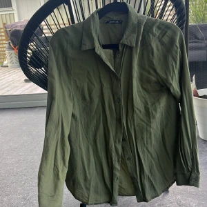 Olivgrön skjorta från Gina Tricot - Olivgrön skjorta från Gina Tricot i 100% viskos. Klassisk krage, knäppning framtill och långa ärmar med manschett. Skjortan har en avslappnad passform och är perfekt för en stilren look. 