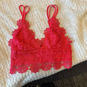 Röd spetsig linnetopp från BikBok - Superfin röd linnetopp från BikBok med tunna axelband och detaljerad spets över hela toppen. Croppad modell med v-ringning och blommigt spetsmönster som ger en romantisk vibe. Perfekt att styla med jeans eller kjol för en trendig look.