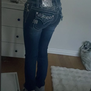 Mörkblå jeans med detaljerade bakfickor - Säljer ett par mörkblå Miss me jeans med snygga broderade och glittriga detaljer på bakfickorna. Jeansen har låg midja, kontrastsömmar och en tight passform som sitter snyggt längs benen. Perfekta för dig som gillar statement-jeans med coola detaljer.