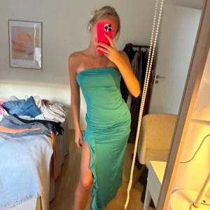 Turkos axelbandslös långklänning - Säljer en turkos axelbandslös långklänning med tight passform och hög slits med volangdetalj. Osäker var den är från då jag köpte på vinted, storlek XS/S