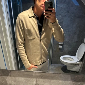 Beige zip-kofta från Samsøe Samsøe - Säljer en stilren beige kofta från Samsøe Samsøe med dragkedja framtill och klassisk krage. Koftan är i mjukt material och har en bröstficka. Skicket på den är bra. Jag är 188cm och den sitter perfekt på mig. Hör av er vid funderingar;)