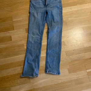 Blå raka jeans från Zara, stl 42 - Säljer ett par klassiska blå jeans från Zara i storlek 42. Jeansen har rak passform, fem fickor och normal midja. Tillverkade i bomull med snygga kontrastsömmar och metallknapp med Zara-logga. Perfekta för en avslappnad och stilren look. 
