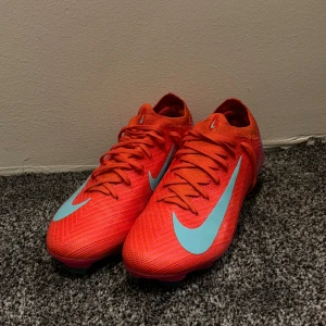 Nike Mercurial fotbollsskor orange/blå - Säljer ett par Nike Mercurial fotbollsskor i en riktigt fet orange färg med ljusblå swoosh och detaljer. Skorna är knappast använda och rätt så nya