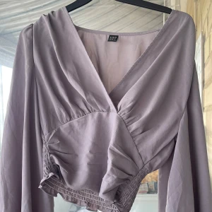 Grå topp från Shein - Supersöt grå omlottopp från SHEIN med v-ringning och långa ärmar. Toppen är croppad med smockad midja och volangkant nertill.