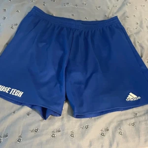 Blå Adidas shorts Climalite L - Säljer ett par blå sportiga Adidas shorts i storlek L med Climalite-teknologi. De har elastisk midja och logga på benet. Perfekta för träning eller fotboll, tillverkade i lätt polyester som andas. Snygg enkel design utan mönster eller extra detaljer.