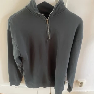Mörkgrå half zip sweatshirt - En stilren mörkgrå sweatshirt med half zip-dragkedja i halsen. Tröjan har lång ärm och en avslappnad passform, perfekt för lager-på-lager. Enkel och clean design som funkar till det mesta.
