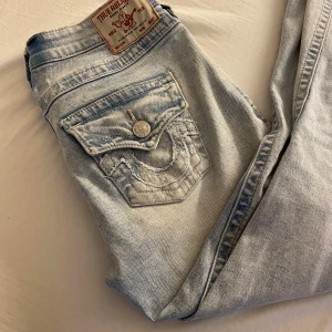 True Religion Joey ljusa flare jeans - Säljer ett par ljusblå True Religion Joey jeans med låg midja och flare-ben. Storlek 25 men är lite insydda!