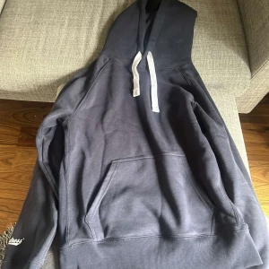 Mörkblå hoodie från Russemerch - Mörkblå hoodie från Russemerch med vit snörning i huvan och stor magficka. Tröjan har lång ärm och logga på ärmslutet. Typ aldrig använd 