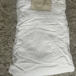 Vita jeansbyxor från Jacob Cohen i modell 622 - Snygga vita jeansbyxor från Jacob Cohen med klassisk femficksdesign och diskret logotyppatch baktill. Byxorna har slim fit och är tillverkade i ett mjukt bomullsmaterial som känns skönt mot huden. Perfekta för en fräsch och stilren look.