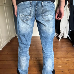 Blå Replay jeans  - Säljer ett par klassiska blå Replay jeans med snyggt slitna detaljer och raka ben. Jeansen har fem fickor, tydliga sömmar och coola bakfickor med dekorativa sömmar. Hör av dig vid frågor eller funderingar!