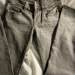 Grå jeans från Perfect Jeans, stl 32 - Snygga grå jeans från Perfect Jeans med raka ben och klassisk femficksdesign. Byxorna har dubbla knappar i midjan och bakfickor med lock och knappdetalj. Perfekt för dig som gillar en stilren look med lite edge. Använd bara en gång 