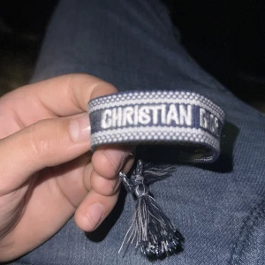 Blått Christian Dior armband med tofsar - Snyggt vävt armband från Christian Dior i blått och vitt med tydlig logga. Armbandet har justerbar knytning och två tofsar i ändarna för en cool och trendig look. Perfekt accessoar för att lyfta din outfit.