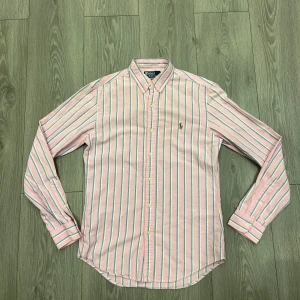 Rosa randig skjorta från Polo Ralph Lauren - Säljer en rosa skjorta från Polo Ralph Lauren med blå och vita ränder. Slim fit-modell med klassisk krage, knäppning framtill och broderad logga på bröstet. Skjortan är i mjuk bomull och har en fräsch, preppy vibe.