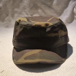 Camo keps i bomull från Army - Snygg militärinspirerad keps i klassiskt camouflage-mönster. Kepsen är tillverkad i slitstark bomull och har en rak, mjuk skärm. Färgerna går i grönt, brunt och beige, perfekt för dig som gillar streetstyle eller outdoor-vibe.