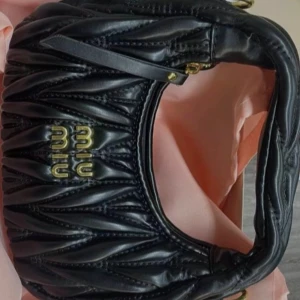 Svart quiltad handväska  - Säljer en svart quiltad handväska från med snygga guldfärgade detaljer och logga framtill. Väskan är tillverkad i skinn och har en cool, vadderad struktur som ger en lyxig känsla. Perfekt accessoar för att lyfta din outfit.