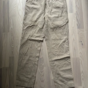 Beiga linnebyxor med snörning - Snygga och luftiga beiga linnebyxor med elastisk midja och snörning framtill. Byxorna har raka ben, sidofickor och bakfickor. 