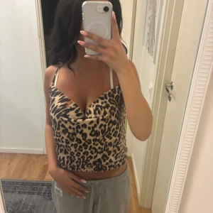 Leopardmönstrad croppad linnetopp - Säljer en croppad linnetopp med leopardmönster och tunna axelband. Toppen har en snygg draperad v-ringning och är i beige och bruna toner. Perfekt för dig som vill sticka ut med ett djuriskt print och en trendig siluett.