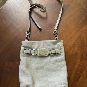 Michael Kors Hamilton crossbody bag - Grå Michael Kors Hamilton crossbody shoulder bag. Ljusgrå handväska i skinn med silverfärgade detaljer. Väskan har en justerbar axelrem och stängs med magnetlås. Inuti finns flera fack, varav ett med dragkedja. Bra skick utöver en söm som spruckit upptill och där den lagats av skomakare, så att detta knappt syns, se bild.  Ca 25x27 cm stor.