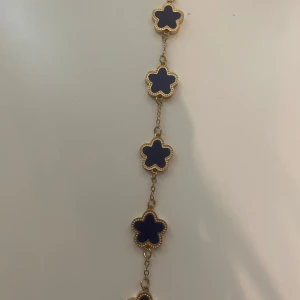 Blått blommigt armband i guldton - Superfint armband med fem blå blommor infattade i guldfärgad metall. Blommorna har en stilren, modern look och armbandet känns både trendigt och elegant. Perfekt accessoar för att lyfta vilken outfit som helst.