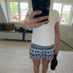 Kort mönstrad kjol i blått och vitt - Supersöt kortkjol med blåvitt mönster och lätt rynkad midja. Kjolen har en luftig känsla och passar perfekt till en enkel t-shirt. Snygg och trendig för dig som gillar att sticka ut lite extra.