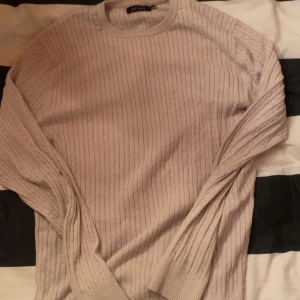 Beige ribbstickad tröja från Riley - Säljer en beige ribbstickad tröja från Riley. Tröjan har rund halsringning, långa ärmar och en klassisk, stilren look. Perfekt för lager-på-lager och passar till många olika outfits.