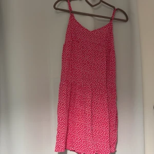 Rosa blommig kortklänning Primark - Supersöt rosa kortklänning från Primark med små vita blommor över hela tyget. Klänningen har smala axelband och en luftig passform, perfekt för varma dagar. Tillverkad i mjuk bomull som känns skön mot huden. Enkel och fräsch stil som passar perfekt till sommaren. Klänningen är liten och skulle är passad till barn runt 10-11 års