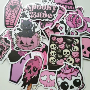 25st Spooky Babe Goth Kawaii Stickers - Snyggt set med 25 st goth-inspirerade klistermärken i rosa och svart. Motiven inkluderar katter, hjärtan, dödskallar, fladdermöss och cupcakes. Perfekt för att dekorera laptops, mobiler eller surfplattor. Alla stickers är i nyskick utan synligt slitage.
