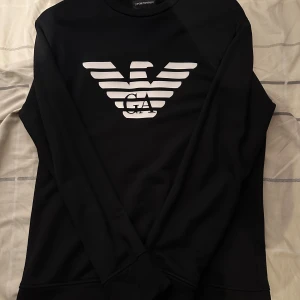 Svart sweatshirt från Emporio Armani - Svart sweatshirt från Emporio Armani med stor vit logga framtill. Klassisk rund halsringning och långa ärmar. kan gå ner i priset vid snabbt köp.