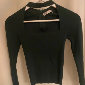 Mörkgrön långärmad topp från ZARA - Snygg mörkgrön långärmad topp från ZARA med fyrkantig urringning och hög krage. Toppen har en stilren design med dragkedja bak och är figurnära i passformen. Perfekt för dig som gillar minimalistisk och modern stil. Använd väldigt få gånger och är därför i mycket bra skick!