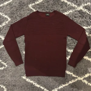 Vinröd ribbad tröja  - Snygg vinröd långärmad tröja från Figo i storlek S. Tröjan har ett ribbat mönster över hela ytan och rund halsringning. Jag är 180cm och väger 68kg och den passar perfekt.