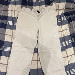 Beige linnebyxor med snörning - Snygga beige linnebyxor med avslappnad passform och elastisk midja med snörning. Byxorna har en bakficka med lock och är perfekta för en chill och stilren look. Luftigt material som passar bra när det är varmt ute.