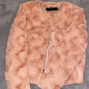 Ljusrosa pälsjacka från Vero Moda - Säljer en fluffig och mjuk ljusrosa pälsjacka från Vero Moda. Jackan har rund hals, långa ärmar och stängs med knappar framtill. Perfekt för dig som vill ha en cozy och trendig look under kyliga dagar. Knappt använd och är i mycket bra skick!