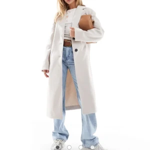 Vit lång kappa med knappar - Snygg lång kappa i ljusvit ton med klassisk krage och svarta knappar framtill. Jackan har raka linjer, sidfickor och är helfodrad. Materialet känns som ullblandning och ger en clean och stilren vibe. Perfekt för dig som gillar minimalistisk och trendig look. Oanvänd 