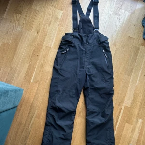 Svarta täckbyxor från Craft - Svarta täckbyxor från Craft med Windstopper-teknologi, justerbara hängslen. Använda 2ggr.