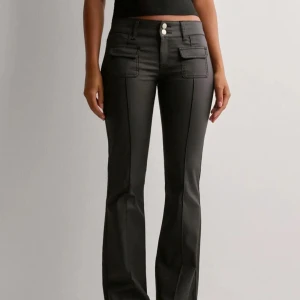 Nelly skinnbyxor  - Snygga svarta bootcut byxor med två framfickor med lock och dubbla knappar i midjan. Byxorna har markerade sömmar längs benen och en stilren look som passar perfekt till en trendig outfit.
