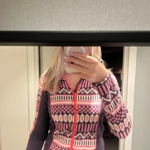 Mönstrad fleecejacka Kari Traa XS - Säljer en snygg fleecejacka från Kari Traa i storlek XS. Jackan har ett färgstarkt geometriskt mönster i rosa, lila och vitt, med orange dragkedja och logga. Långärmad och med hög krage, perfekt för kyliga dagar. Supermjuk och skön att ha på sig!