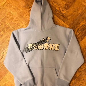 Ljusblå hoodie från Demont XL - Snygg ljusblå hoodie från Demont i storlek XL med stort broderat logotryck och stjärndetaljer på bröstet. Tröjan har huva, magficka och ribbade muddar. Perfekt för dig som gillar streetwear och vill ha en chill look. Sparsamt använd.