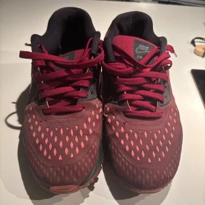 Nike Air Max vinröda sneakers - Säljer ett par Nike Air Max sneakers i vinrött med svarta detaljer och svarta sulor. Skorna har snygga mönstrade meshpaneler och klassisk Air Max-dämpning. De har snörning och en sportig vibe, perfekta för dig som gillar streetstyle och komfort.