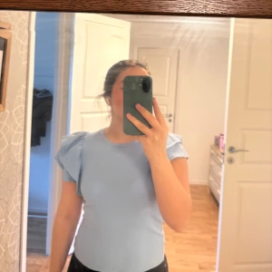Ljusblå ribbad topp med volangärmar från Zara - Superfin ljusblå topp från Zara med ribbad struktur och korta volangärmar som ger en extra touch. Modellen är slim och har rund halsringning. Perfekt att styla med jeans eller kjol för en trendig look. Materialet känns mjukt och stretchigt. Allt ska bort så accepterar alla rimliga bud🌸