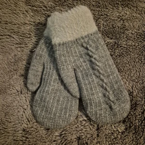 Grå stickade vantar med fluffig kant - Mysiga grå stickade vantar med fluffig, ljusgrå kant upptill. Vantarna har ett klassiskt flätmönster på ovansidan och är perfekta för kalla dagar. Materialet är mjukt och värmande, och den stickade strukturen ger en skön känsla. Dessa är fodrade med mjuk fleece.