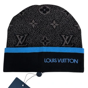 Louis Vuitton svart och blå mössa - Snygg svart mössa från Louis Vuitton med klassiskt monogrammönster i grått och en blå kant. Broderad Louis Vuitton-logga framtill. Tillverkad i mjukt stickat material som håller dig varm och stilsäker under kalla dagar.