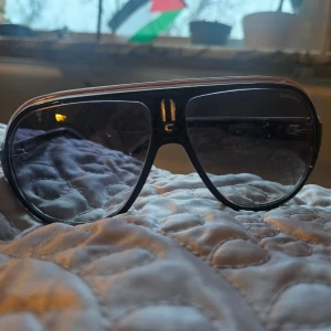 Svarta Carrera Speedway solglasögon - Snygga svarta Carrera Speedway solglasögon med breda bågar och klassisk aviatorform. Glasen är mörka och ramen har en diskret silverdetalj upptill. Modellen heter Speedway Keelf och har en cool retrovibe som sticker ut.