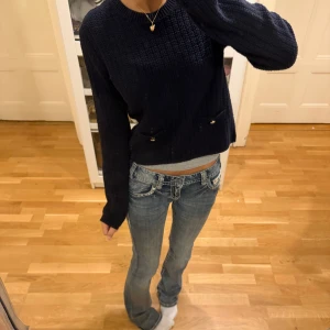 Mörkblå stickad tröja från H&M XS - Snygg mörkblå stickad tröja från H&M i storlek XS. Tröjan har två små fickor framtill med guldfärgade knappar som detalj. Modellen är med rund hals och långa ärmar, perfekt för att ge en chill och trendig vibe till din outfit.