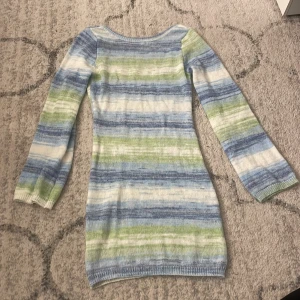 Randig stickad klänning i blått och grönt - Superfin stickad klänning med långa ärmar och rundad urringning i ryggen. Mjuka blå, gröna och vita ränder ger en fräsch och chill vibe. Perfekt för dig som gillar en avslappnad men ändå snygg look. Materialet är stickat och känns lätt mot huden.