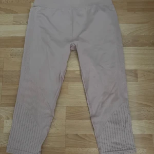 Ljusrosa ribbade träning capri leggings - Snygga ljusrosa leggings med ribbade detaljer längs sidorna och nedre delen av benen. De har hög midja och är tillverkade i ett stretchigt syntetmaterial som sitter tight och bekvämt. Perfekta för träning eller chill dagar.