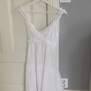 Vit somrig klänning från RYVLS - Superfin vit klänning från RYVLS med volangdetaljer och omlott-v-ringning. Klänningen har breda axelband med volanger och är ärmlös. Endast använd 1 gång! 🥰köpte för 400kr 