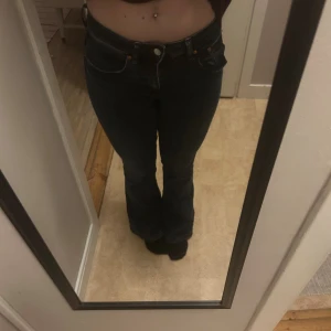 Mörkblå bootcut jeans - Snygga mörkblå jeans med bootcut passform och klassisk femficksdesign. Jeansen har låg midja och är tillverkade i ett stretchigt denim-material som sitter bekvämt. Perfekta för dig som gillar en retro vibe och vill ha ett par jeans som framhäver benen.